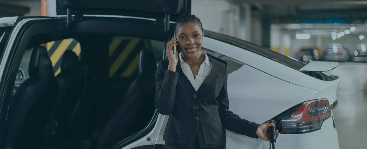 Woman charing her electric SUV in her EVAL certified workplace parking lot while taking a business call